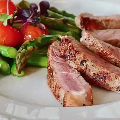 Juicy grilled steak with fresh vegetables on white plate, delicious fine dining image.