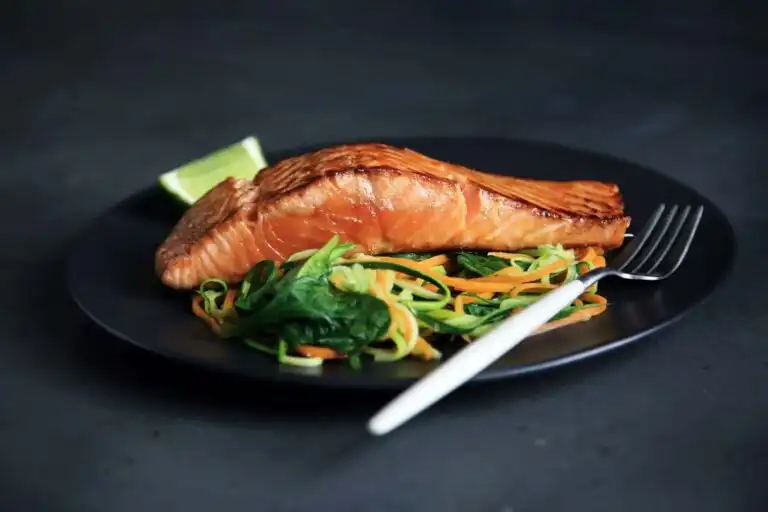 Fresh cooked salmon with vegetable noodles and lime wedge on black plate.