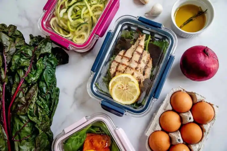 Fresh meal prep with grilled chicken, fresh vegetables, and eggs on a white marble surface.