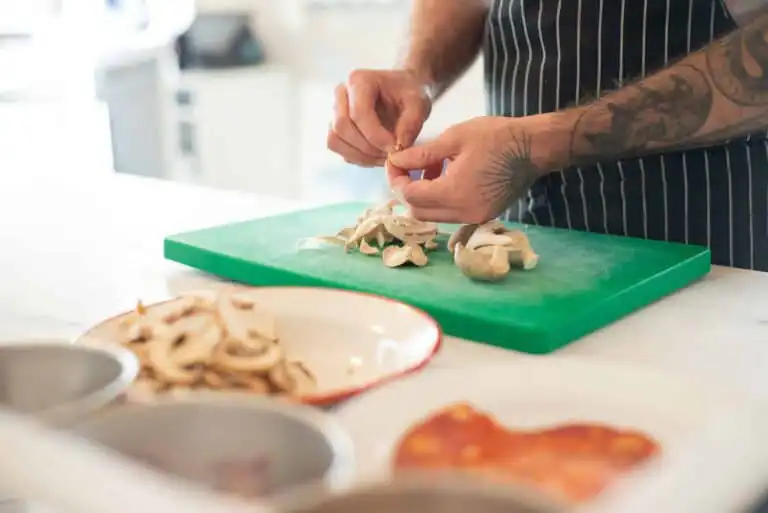 Fresh mushrooms being sliced on a green cutting board in a modern kitchen.